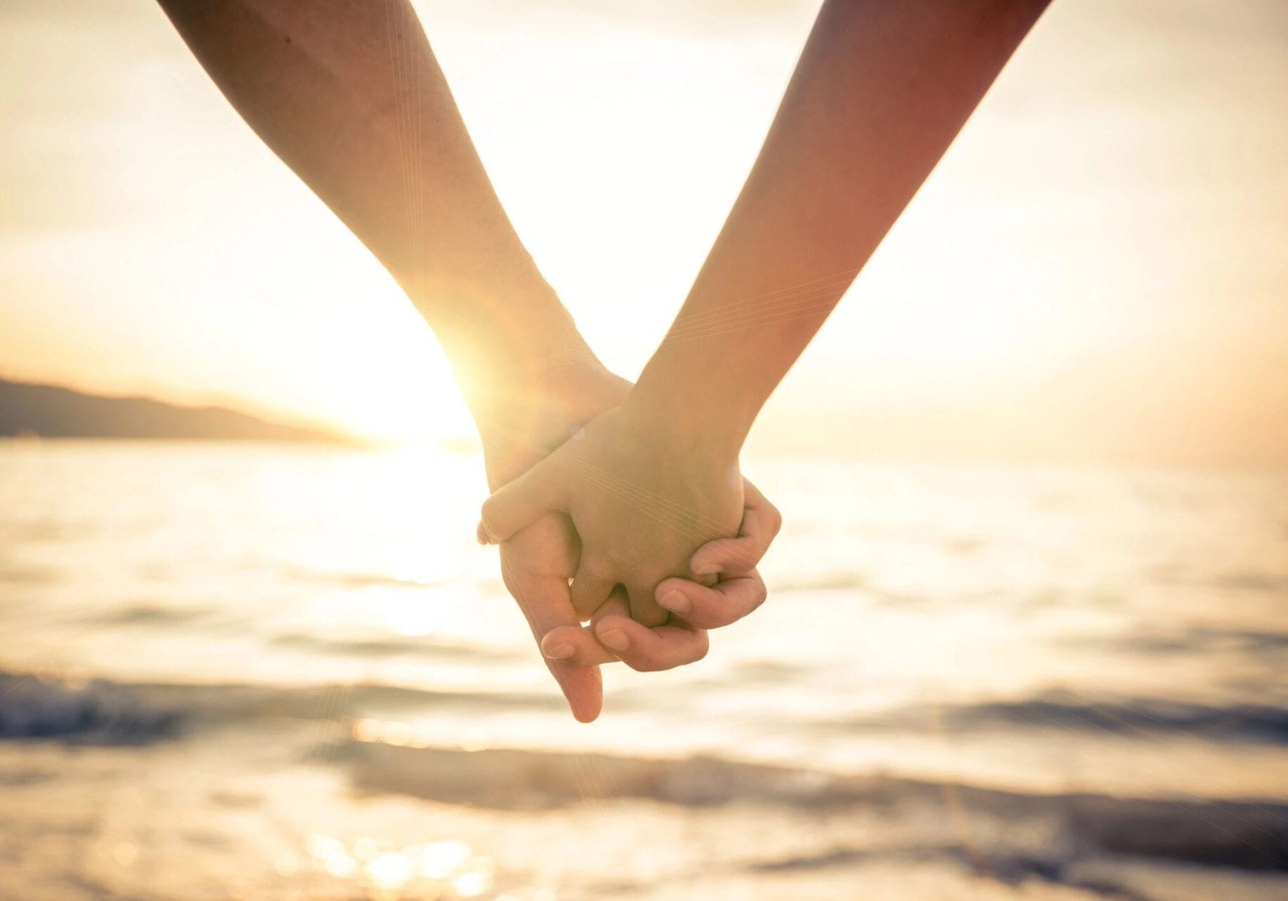 Two people holding hands in front of the ocean.