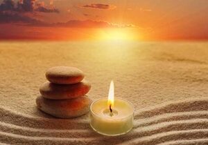 A candle and rocks in the sand at sunset.